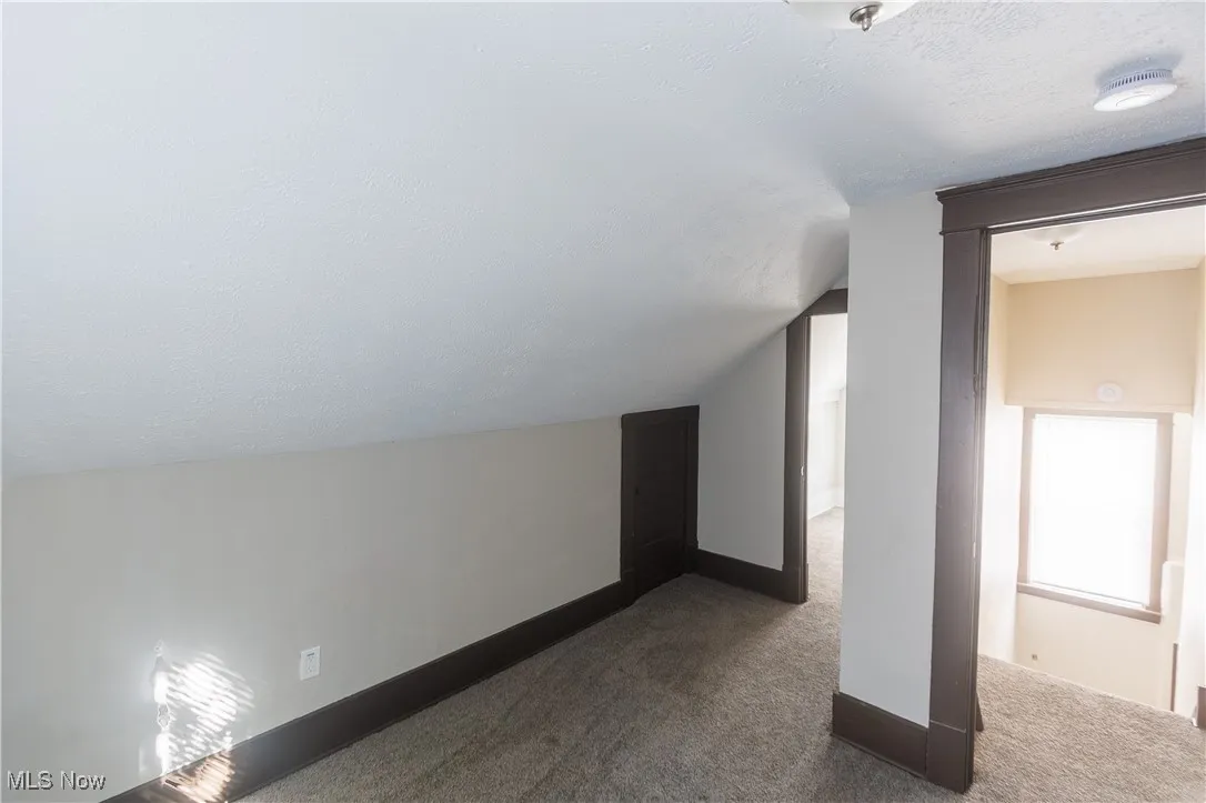 Bonus room with a textured ceiling, dark colored carpet, and lofted ceiling