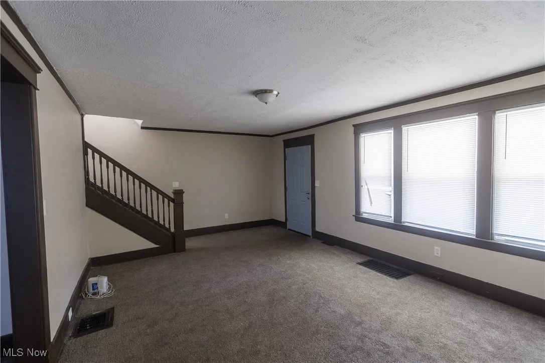 Unfurnished living room with a textured ceiling, carpet, stairway, and ornamental molding