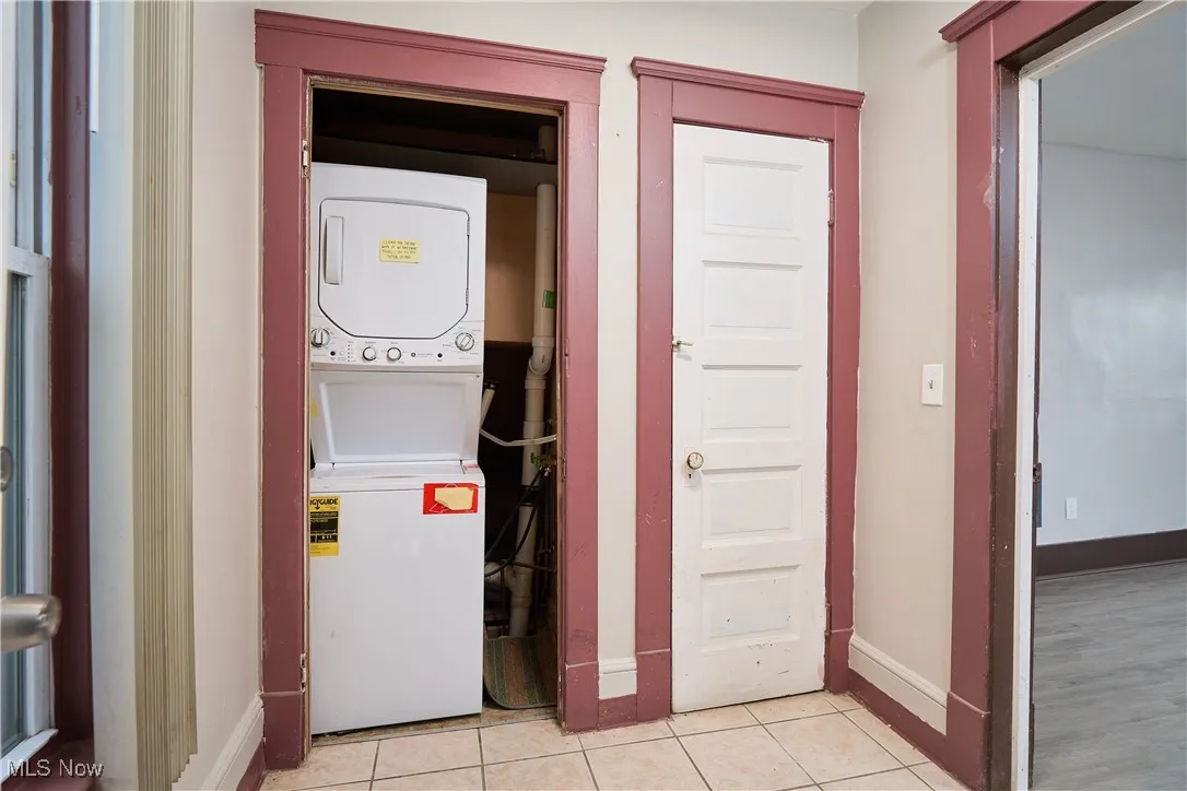 Washroom with stacked washer / dryer and light tile patterned floors