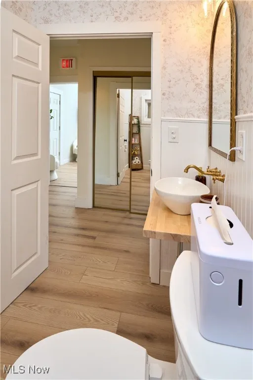 Half bath featuring wallpapered walls, light wood finished floors, vanity, and wainscoting