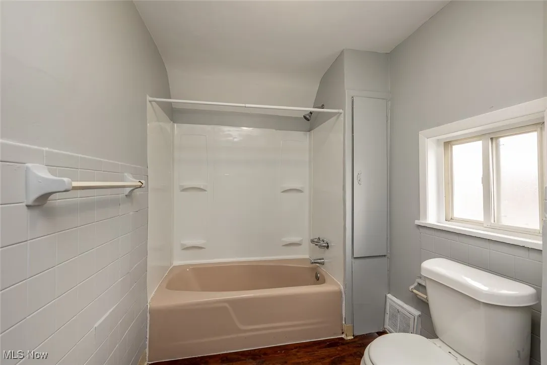 Bathroom with tile walls, tub / shower combination, dark wood-style floors, and wainscoting