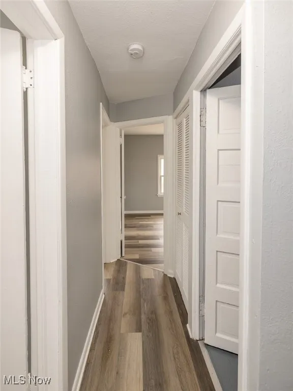 Corridor featuring dark wood-type flooring, a textured wall, and a textured ceiling