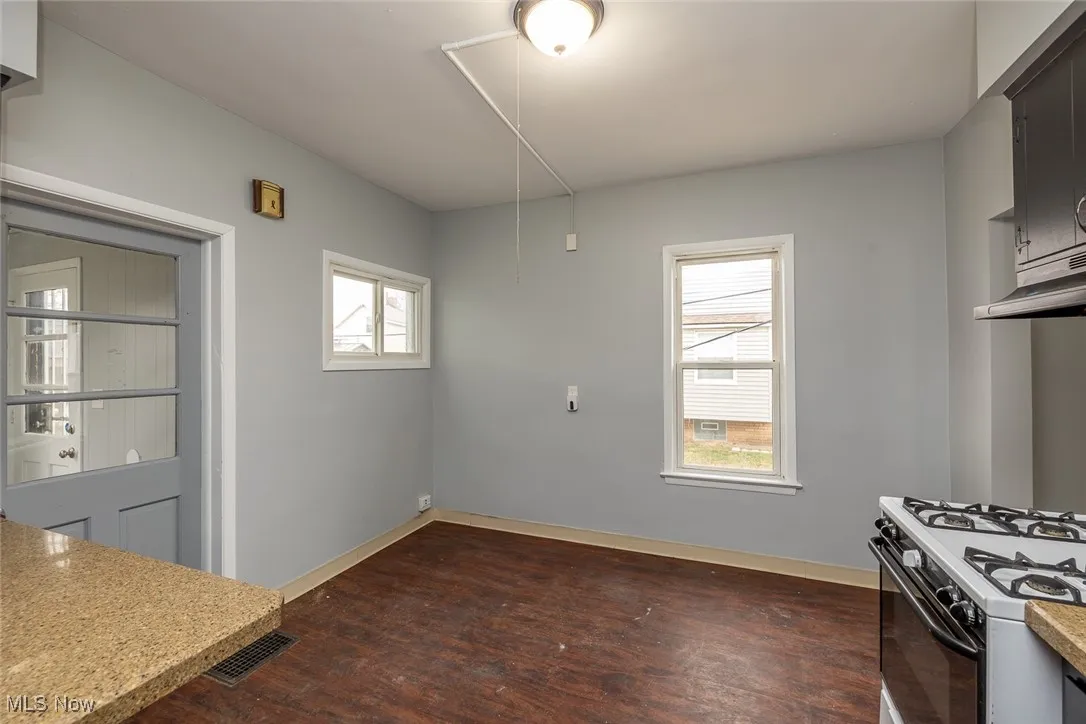 Kitchen with dark wood finished floors, white gas stove, light stone counters, and under cabinet range hood