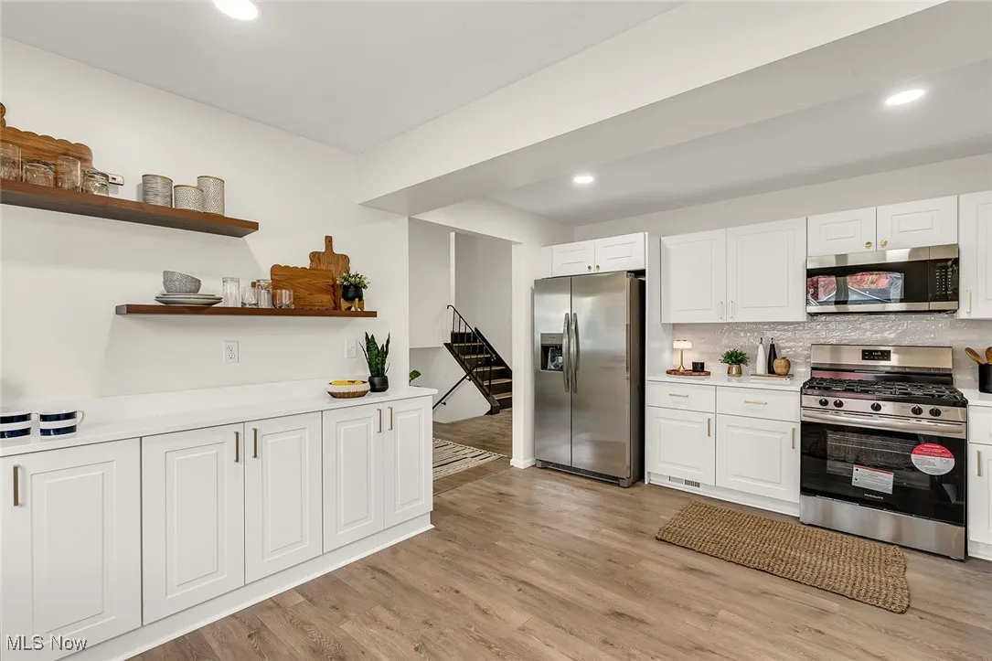 Kitchen featuring stainless steel appliances, tasteful backsplash, white cabinets, open shelves, and light wood-style flooring