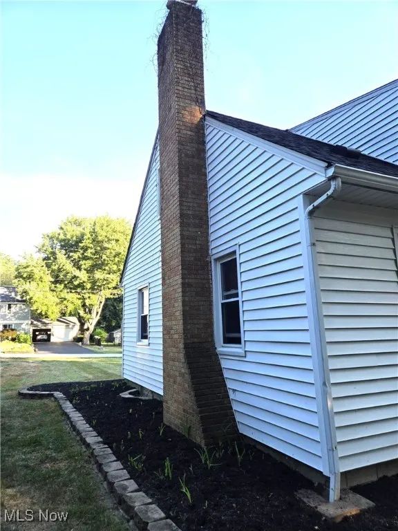View of side of property with a brick chimney. View of pavers and landscaped yard.