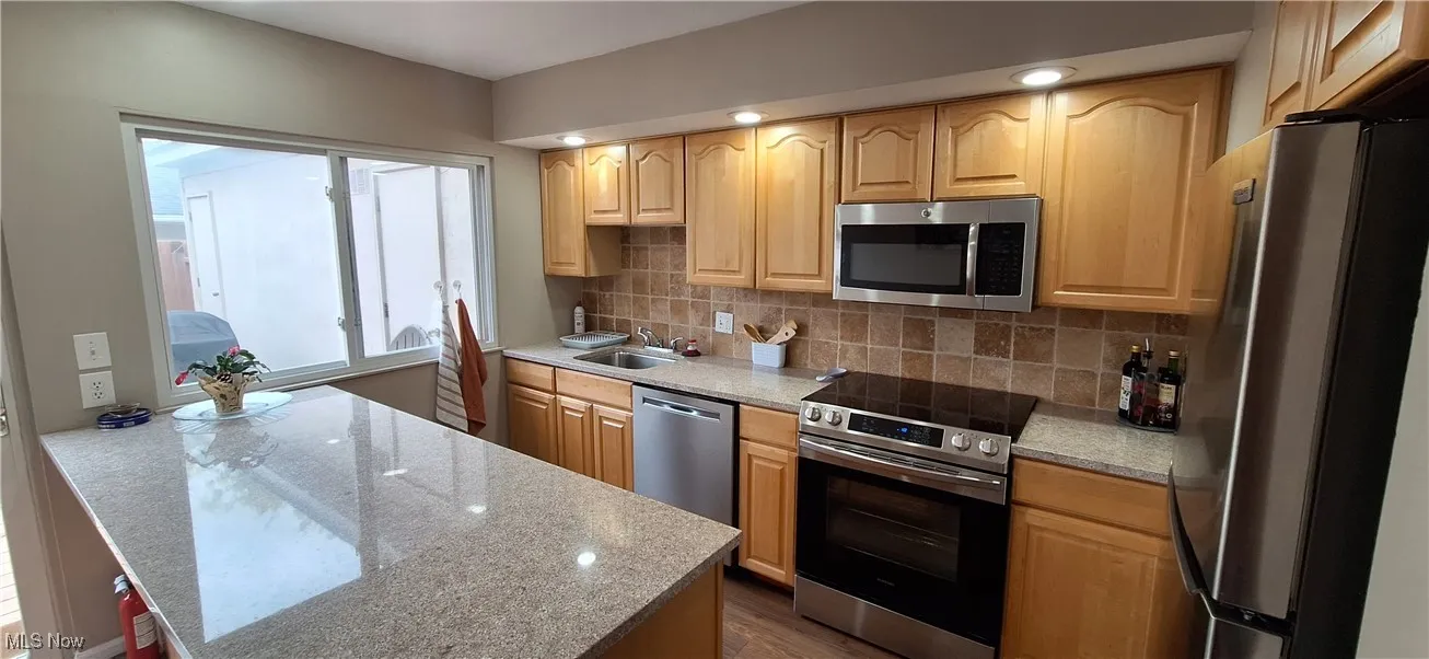Kitchen with stainless steel appliances, tasteful backsplash, dark wood-style flooring, light stone countertops, and light brown cabinets
