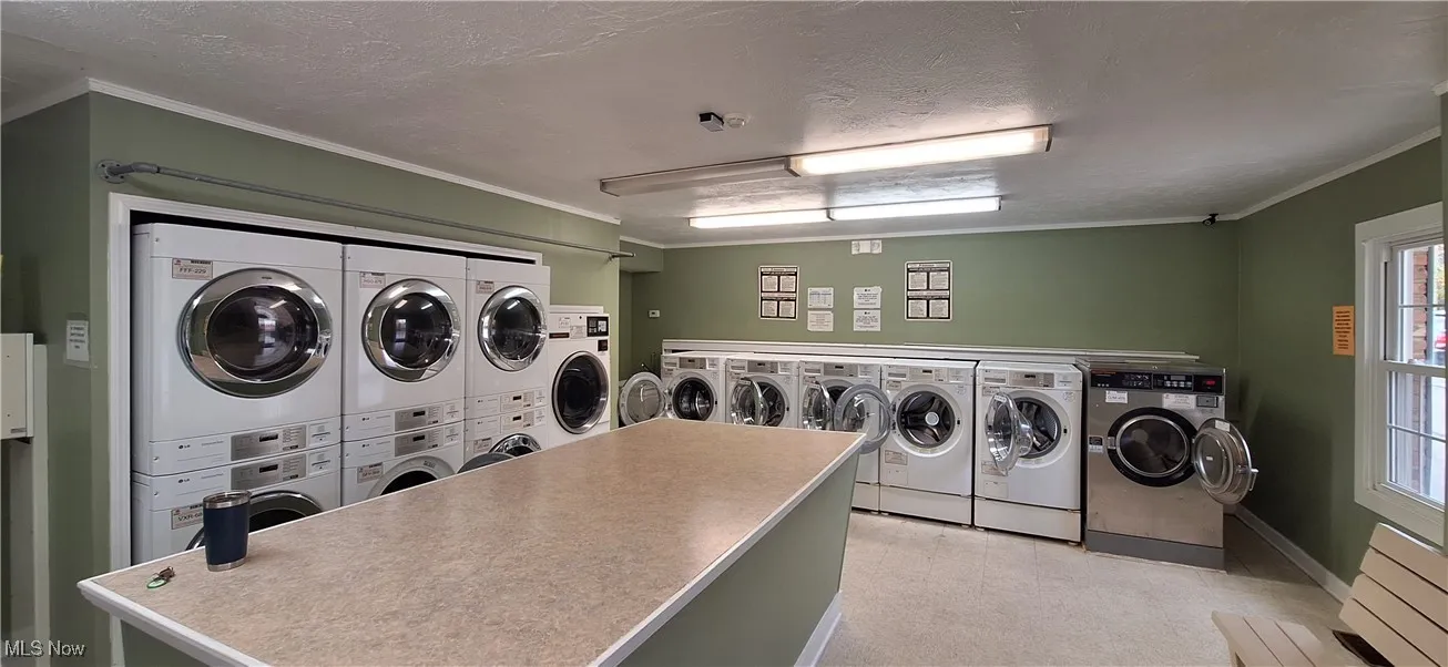 Washroom featuring a textured ceiling, ornamental molding, washing machine and dryer, and radiator