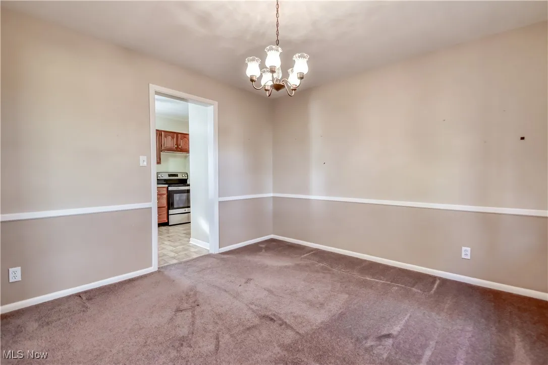 Empty room with light colored carpet and a chandelier