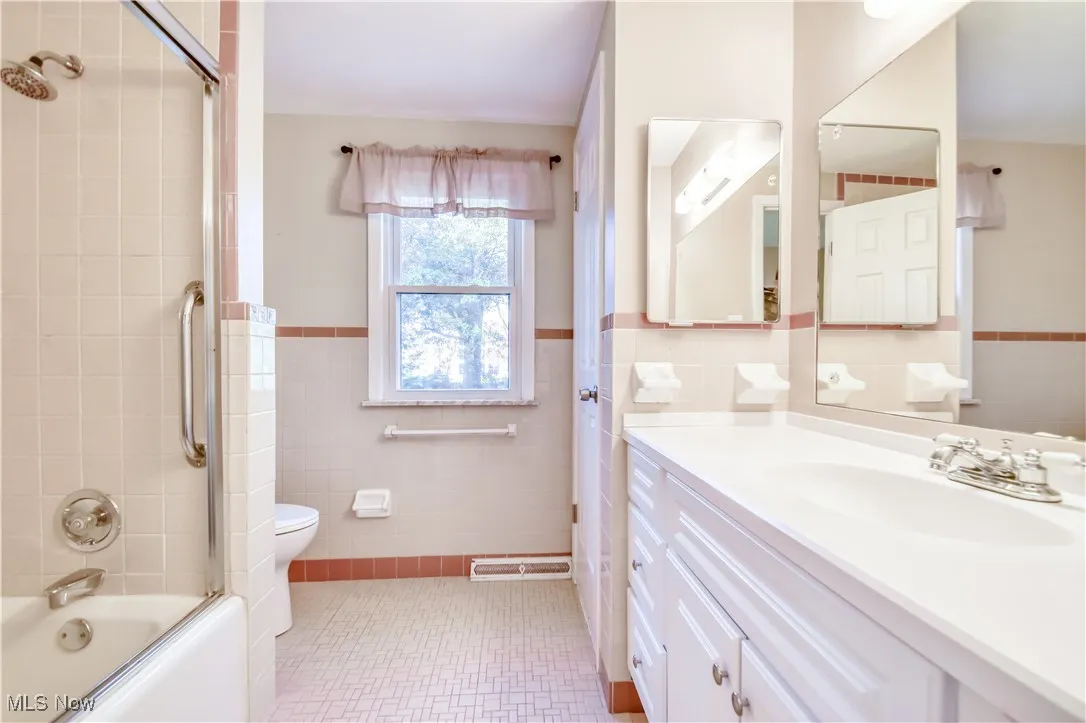 Full bath with tile walls, vanity, a wainscoted wall, and enclosed tub / shower combo