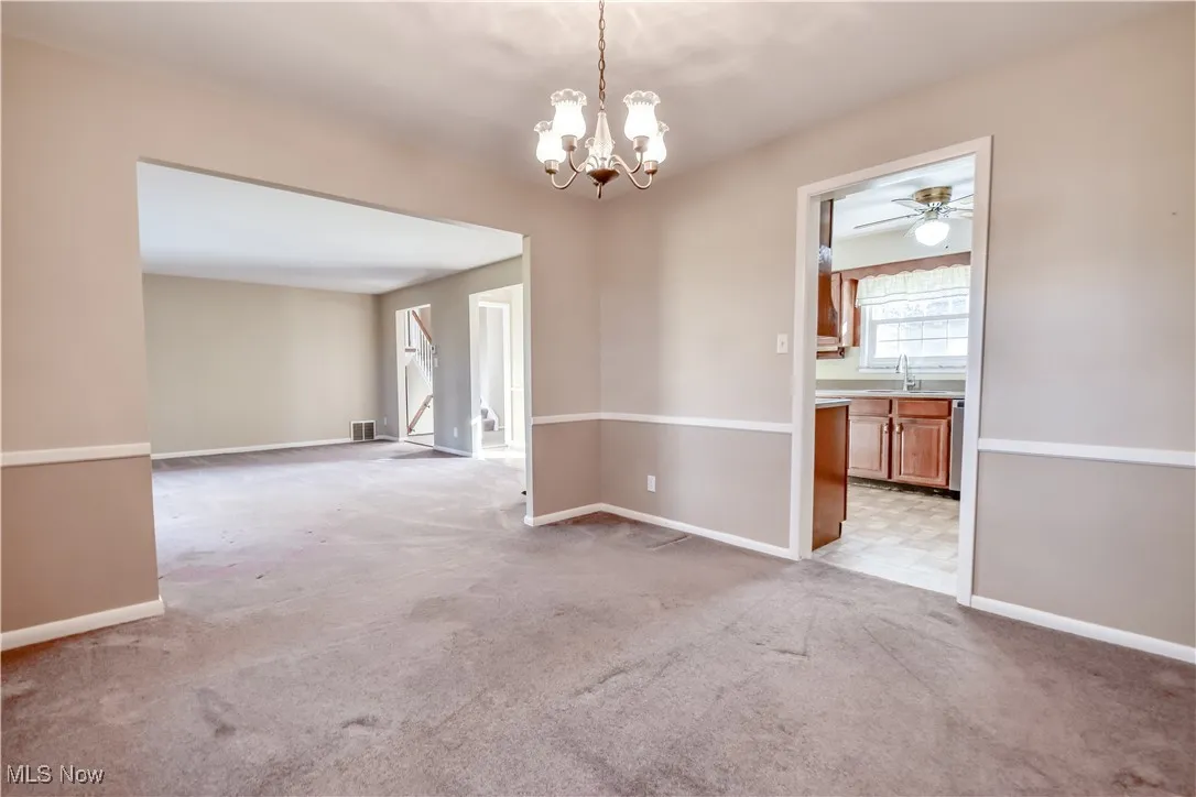 Spare room featuring light colored carpet, a chandelier, and ceiling fan