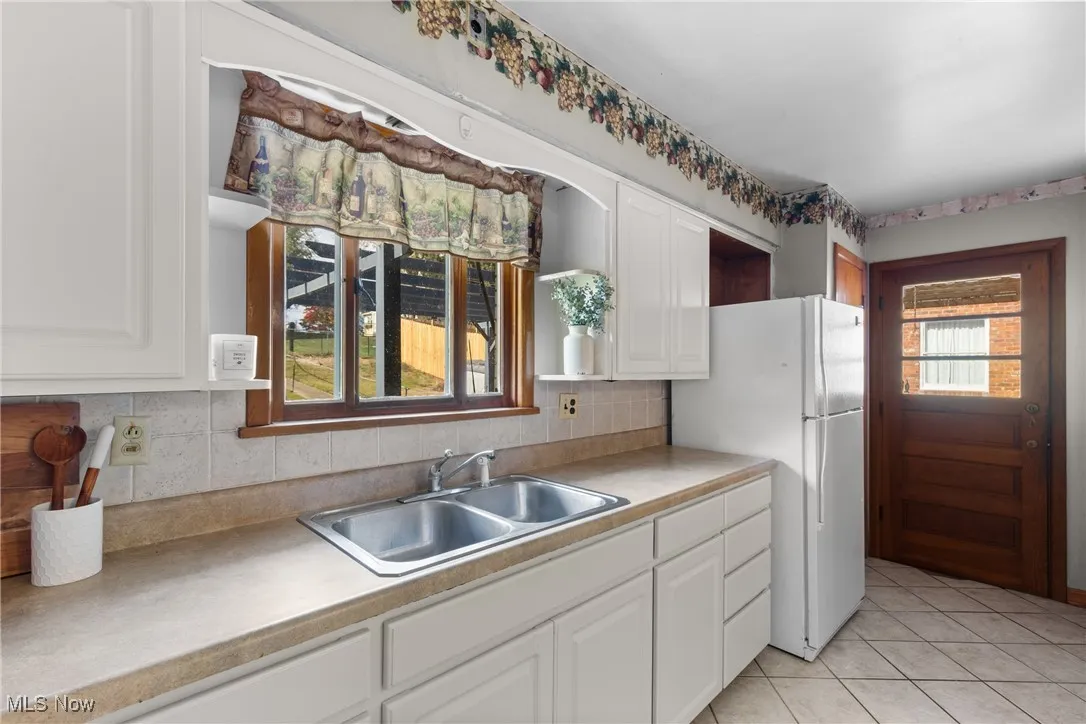 Kitchen featuring white cabinets, light tile patterned floors, freestanding refrigerator, and decorative backsplash