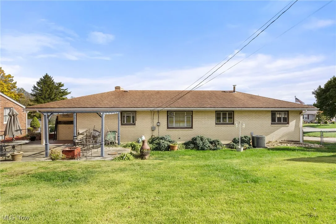 Rear view of house featuring brick siding, a chimney, a patio, and a shingled roof