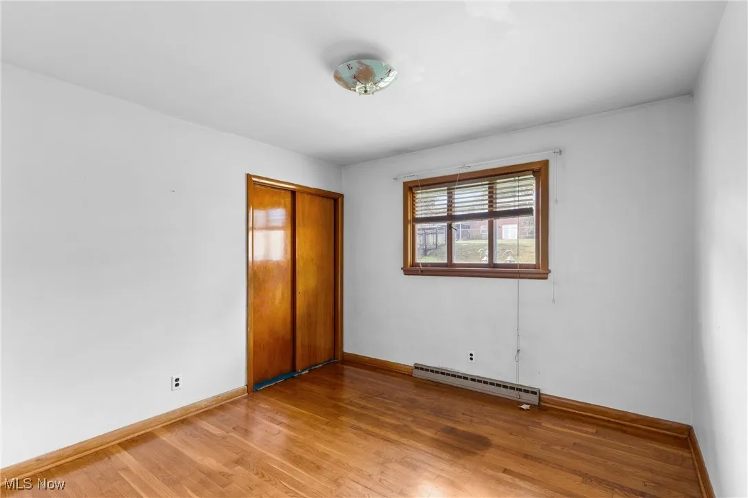 Unfurnished bedroom featuring light wood-type flooring, a closet, and baseboard heating