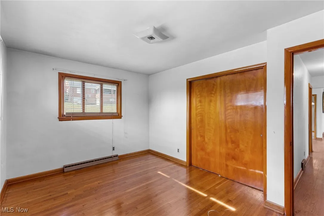 Unfurnished bedroom featuring hardwood / wood-style flooring, a closet, and a baseboard radiator