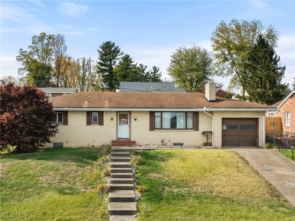Ranch-style home featuring a front lawn, driveway, a garage, and a chimney