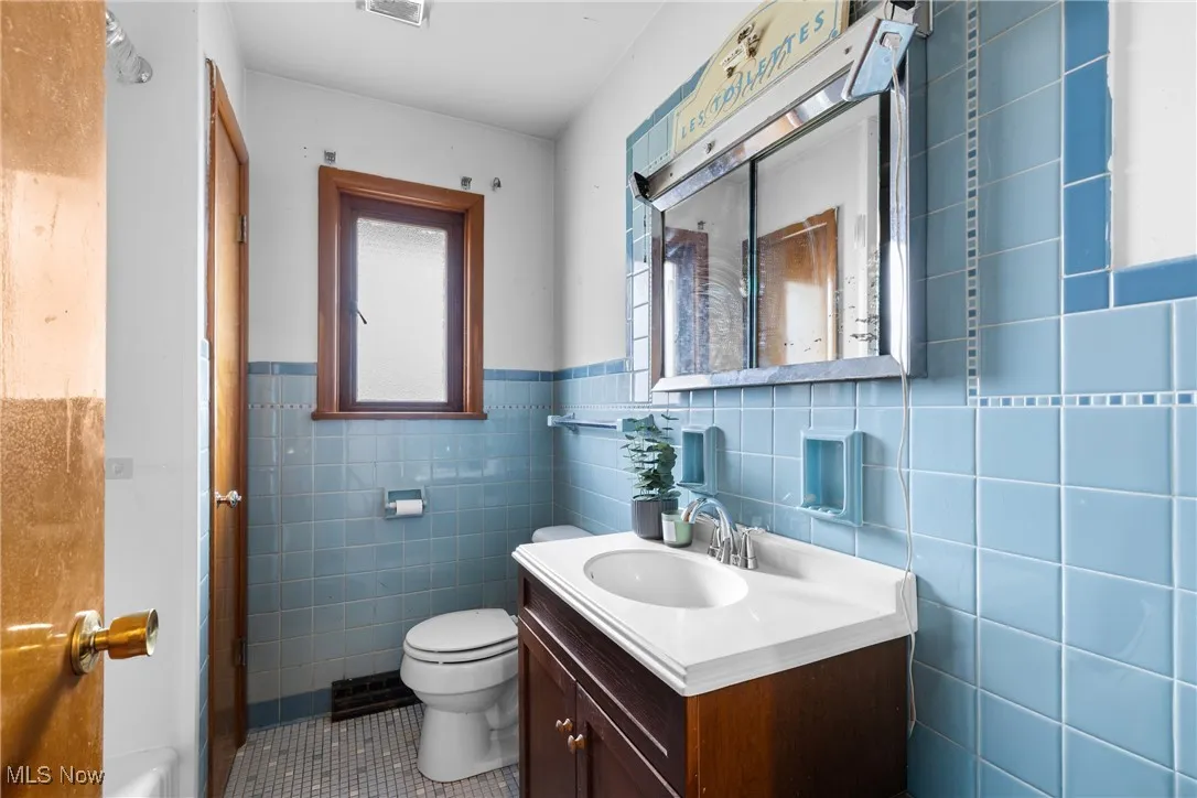 Bathroom with vanity, tile walls, dark tile patterned floors, and wainscoting