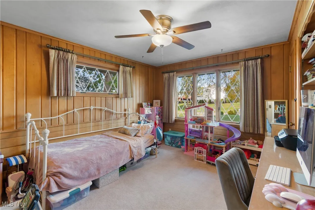 Carpeted bedroom featuring wood walls and a ceiling fan