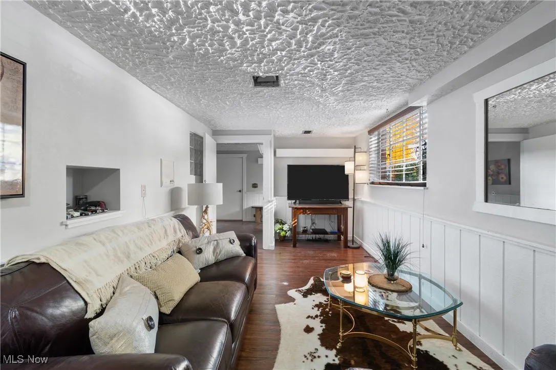 Living area with dark wood-style floors, a textured ceiling, and a wainscoted wall