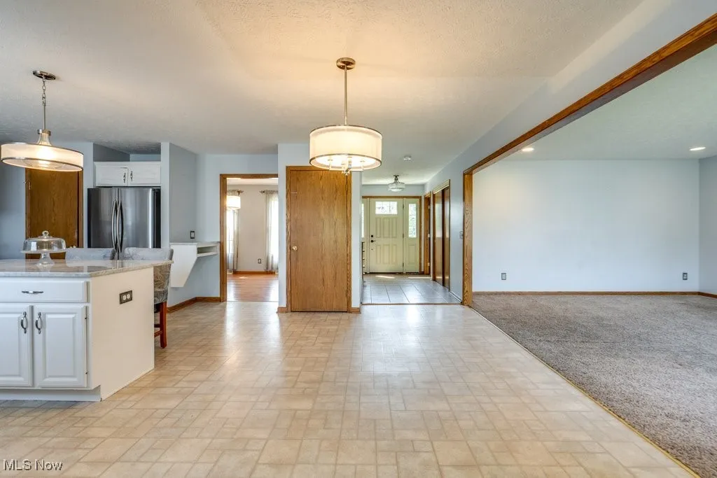 Kitchen featuring tasteful backsplash, a breakfast bar area, white cabinets, light stone countertops, and decorative light fixtures
