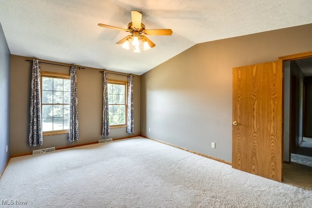 Spare room with carpet flooring, a textured ceiling, vaulted ceiling, and a ceiling fan