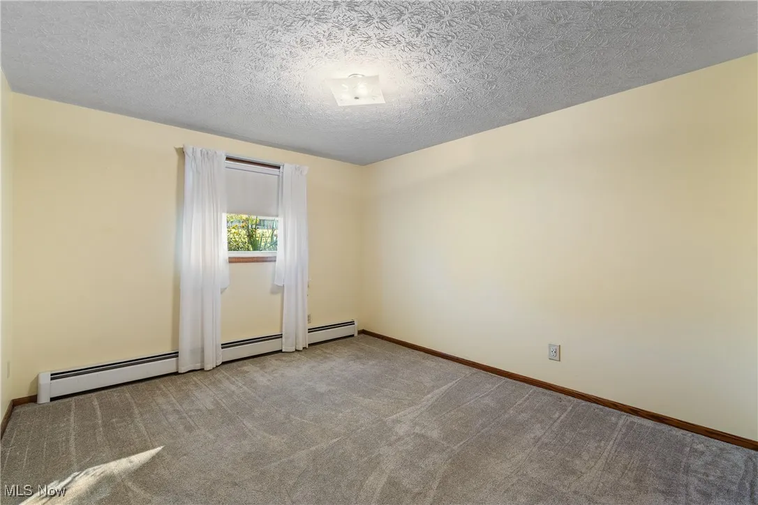 Spare room featuring a textured ceiling, light colored carpet, and baseboard heating