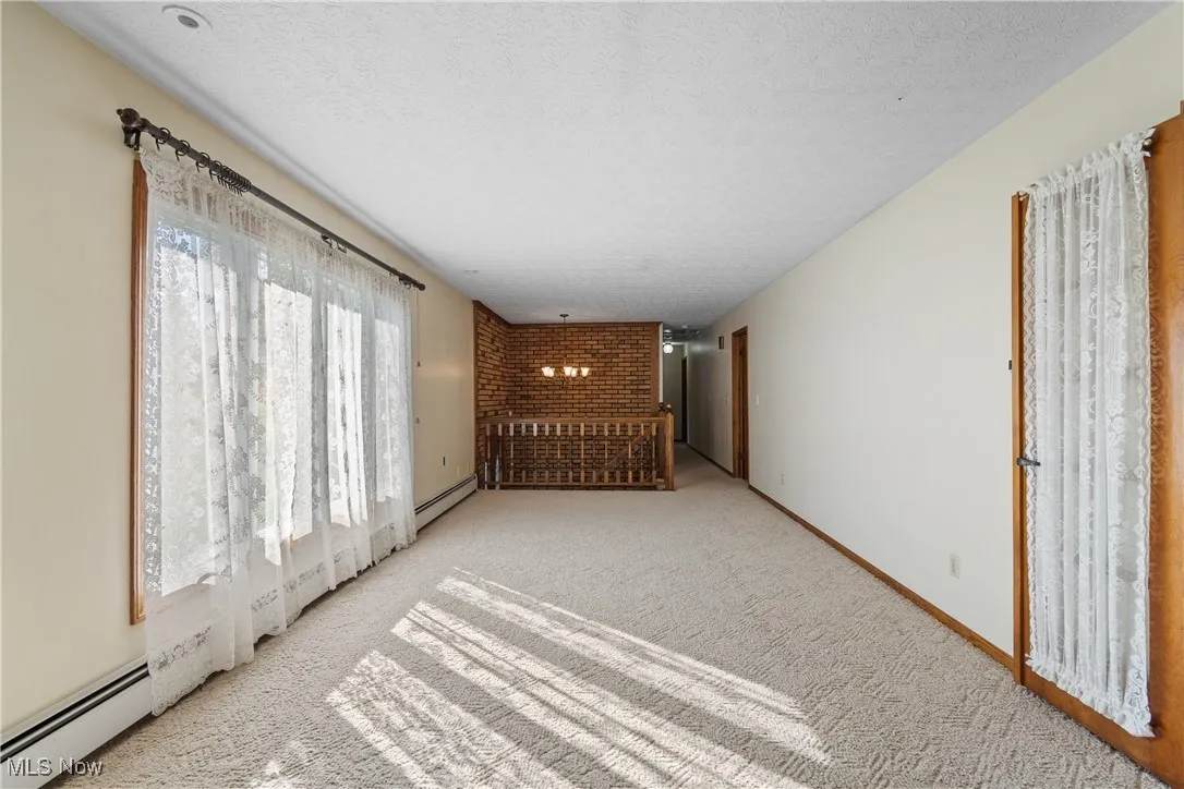 Hallway featuring a textured ceiling, a chandelier, a baseboard radiator, and carpet