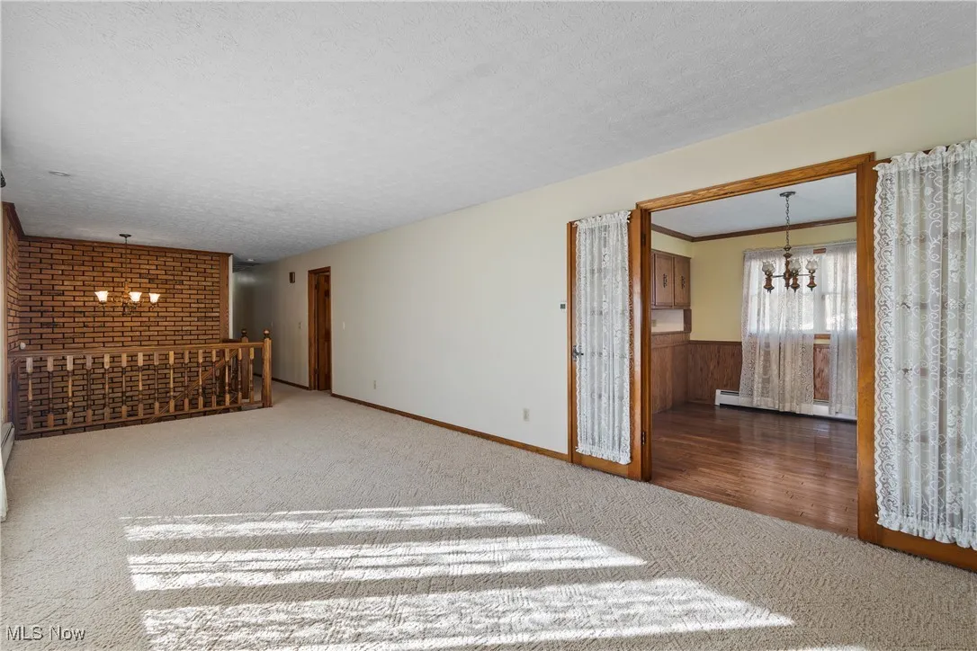 Unfurnished living room featuring a chandelier, carpet, a textured ceiling, a baseboard heating unit, and wood walls