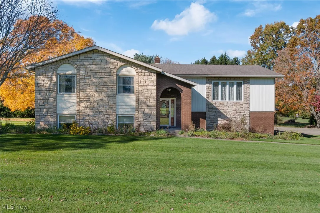 View of front of property with stone siding, a front yard, and a chimney