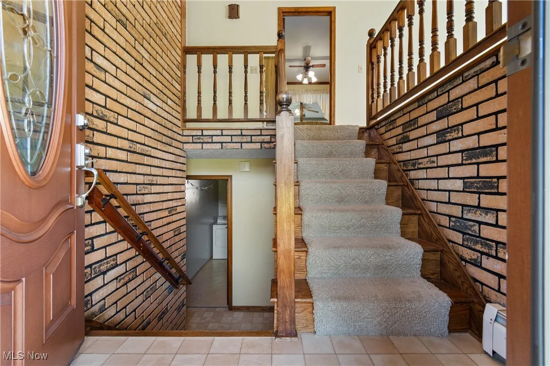 Stairway with tile patterned flooring, baseboard heating, washer / clothes dryer, and brick wall