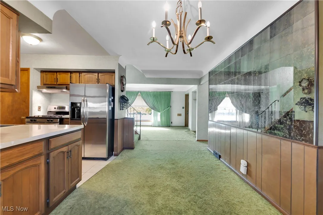 Kitchen featuring appliances with stainless steel finishes, light colored carpet, brown cabinets, a chandelier, and light tile patterned​​‌​​​​‌​​‌‌​‌‌​​​‌‌​‌​‌​‌​​​‌​​ floors