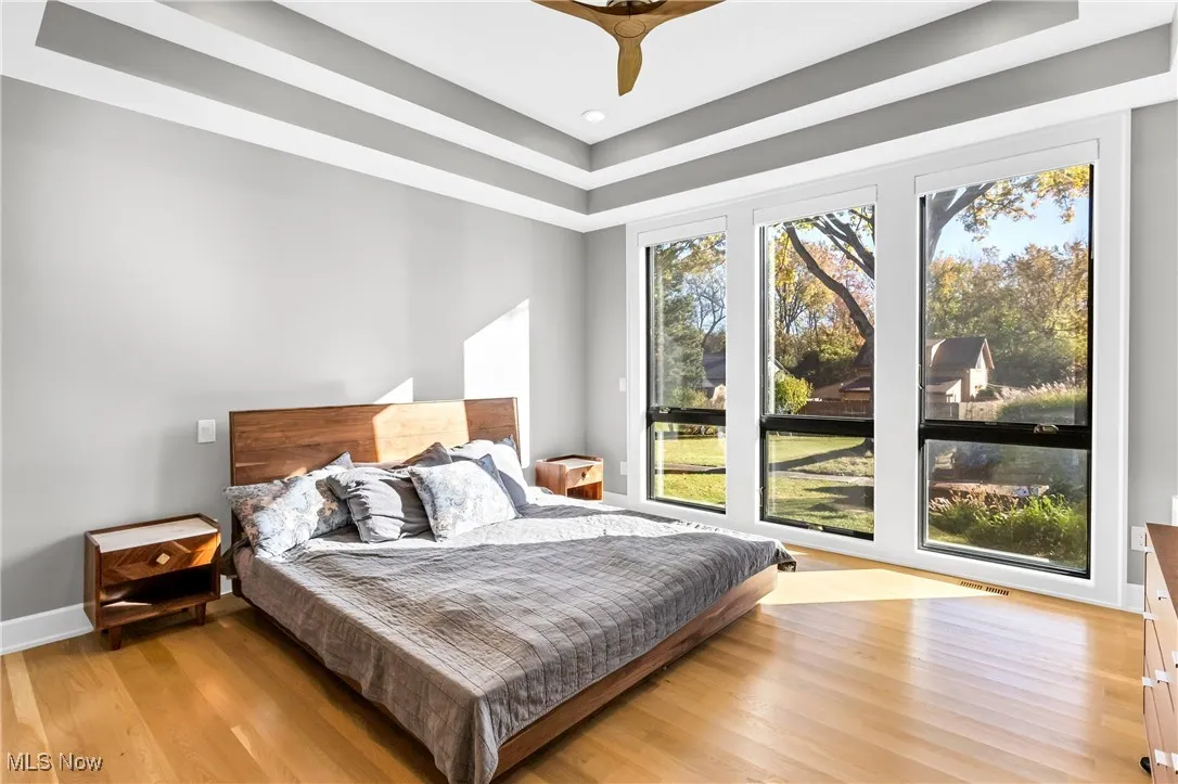Bedroom with a tray ceiling, light wood-type flooring, and ceiling fan