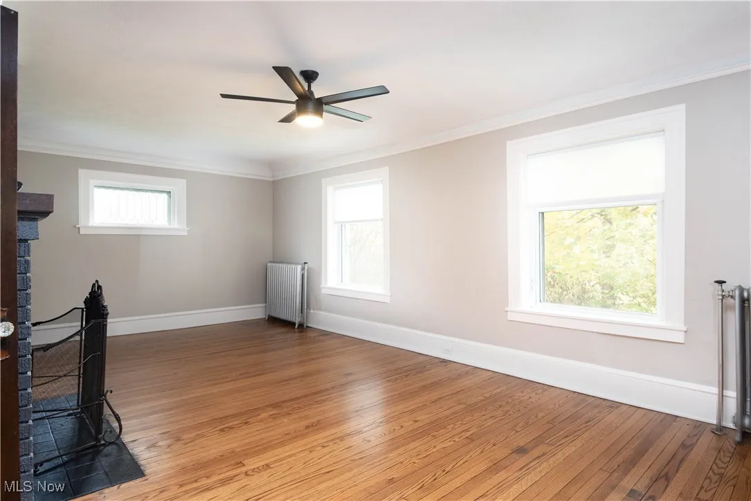 Unfurnished living room featuring crown molding, hardwood / wood-style floors, radiator heating unit, radiator, and ceiling fan