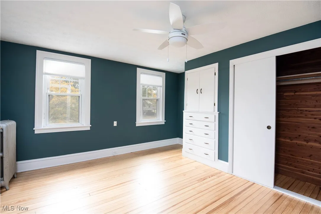 Unfurnished bedroom featuring radiator heating unit, light wood-style floors, ceiling fan, and a closet