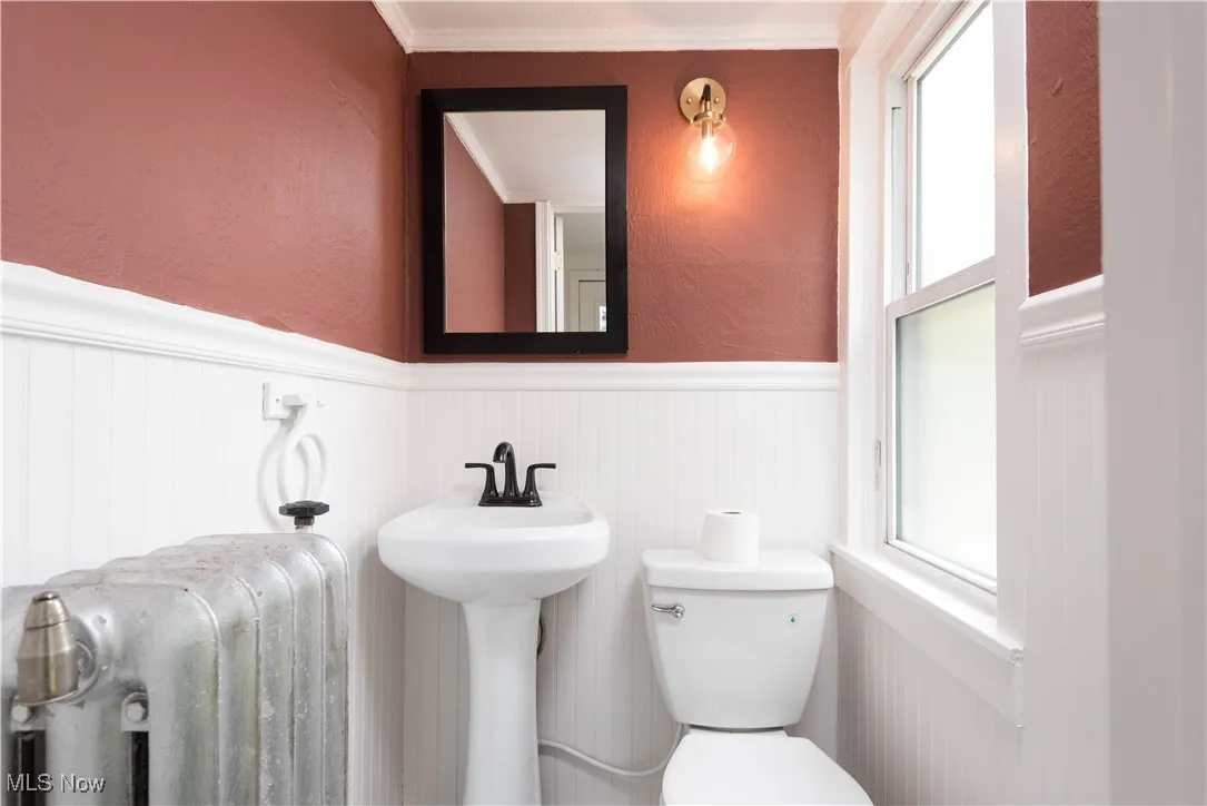 Half bathroom with a textured wall, a wainscoted wall, radiator heating unit, and ornamental molding