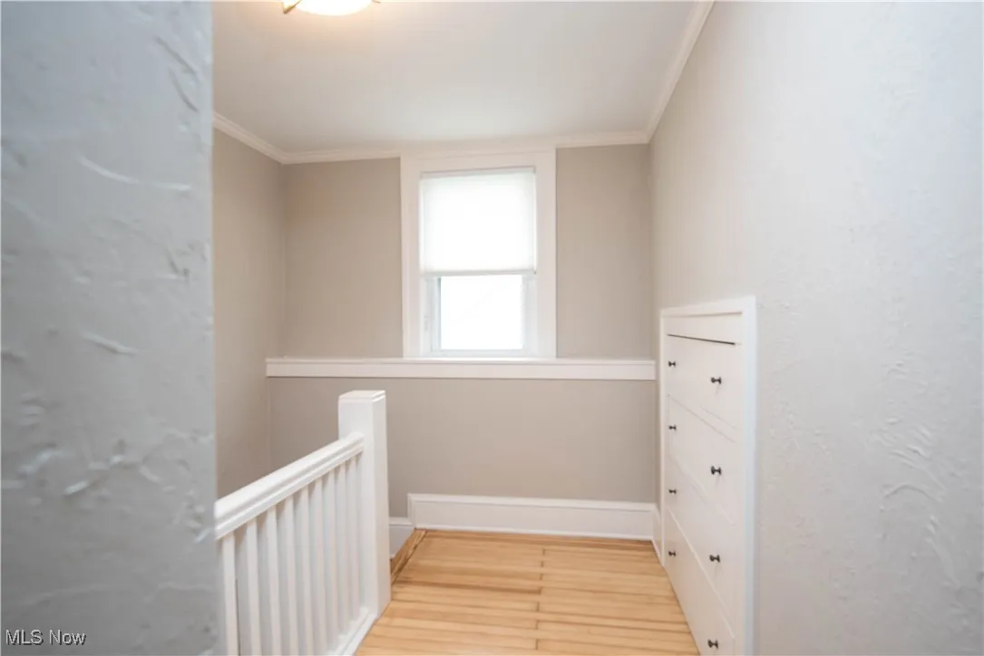 Hallway featuring crown molding, a textured wall, and light wood finished floors