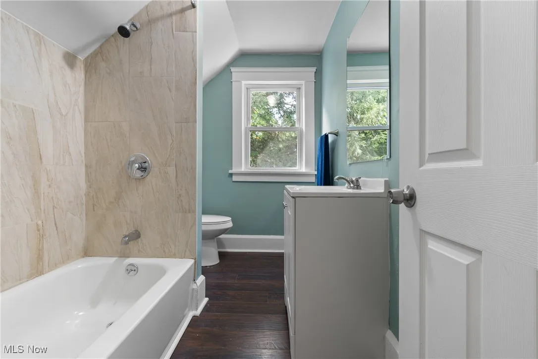 Bathroom featuring vanity, shower / tub combination, dark wood-type flooring, and vaulted ceiling