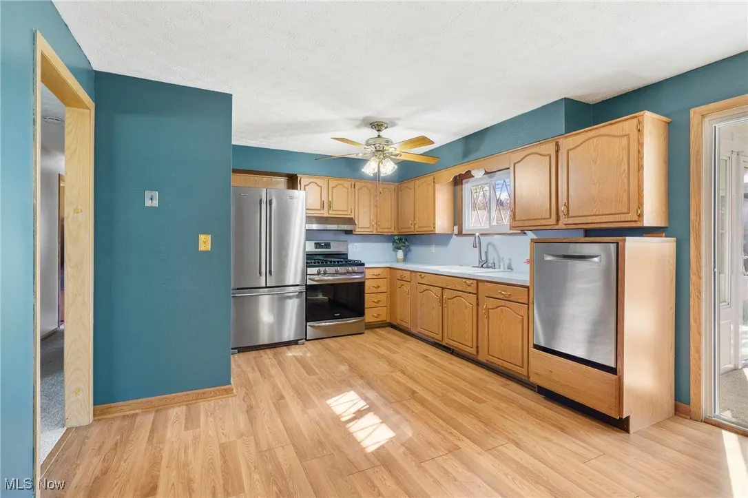 Kitchen with stainless steel appliances, light countertops, a ceiling fan, light wood-style flooring, and light brown cabinetry