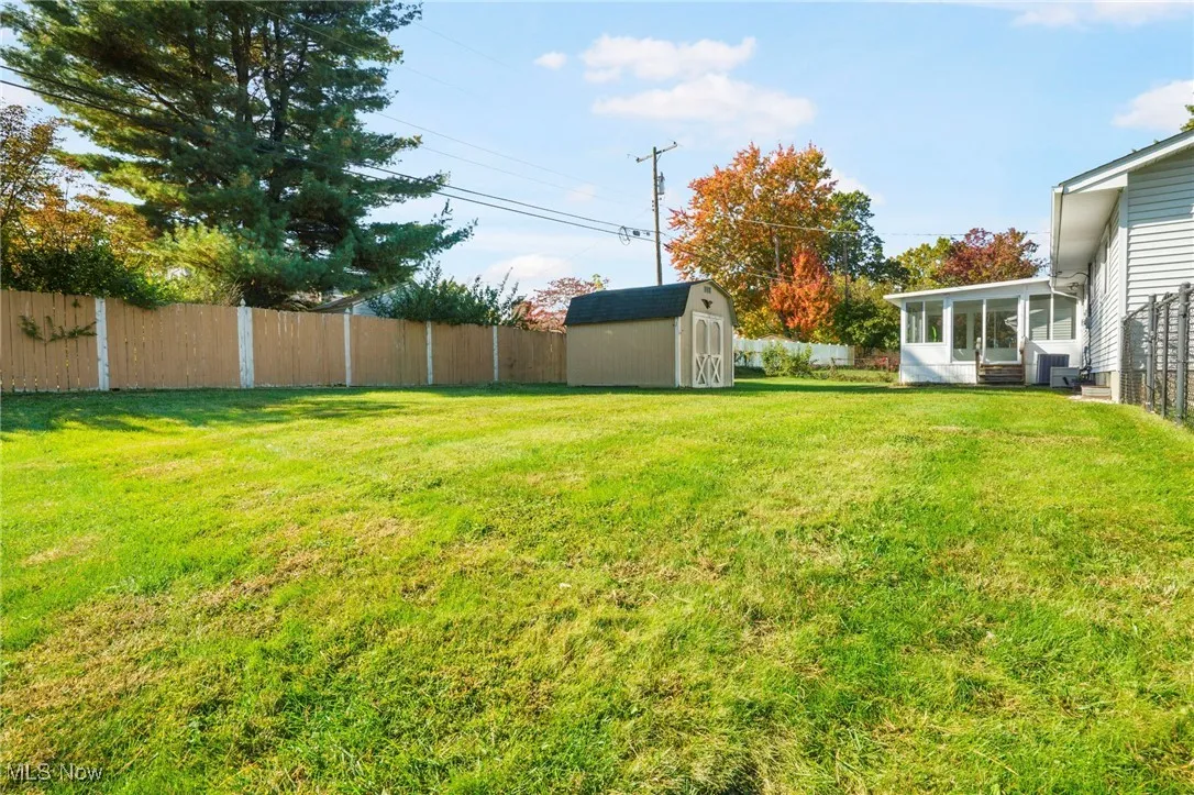 Fenced backyard featuring a sunroom and a storage shed