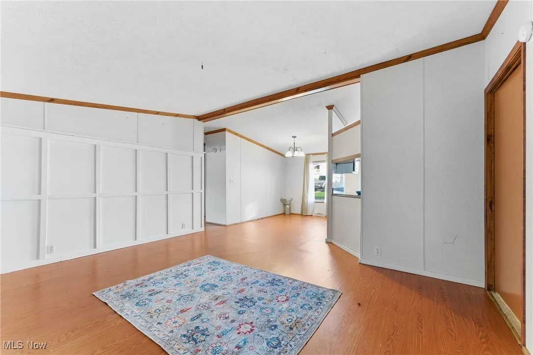 Unfurnished living room with crown molding, light wood finished floors, a decorative wall, and beamed ceiling