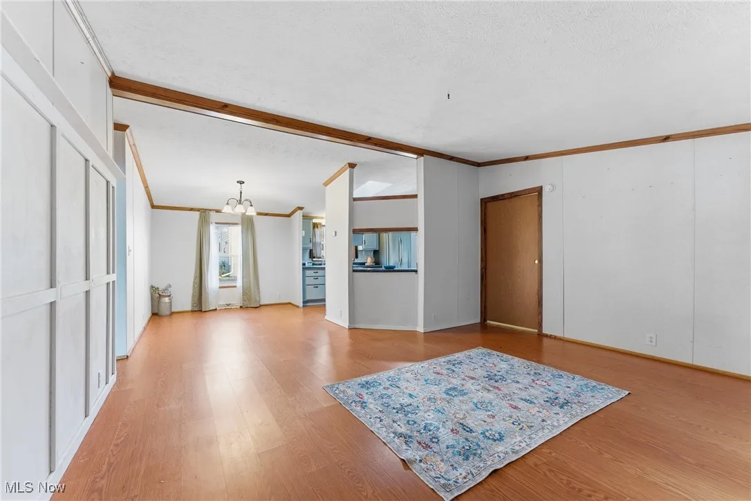 Unfurnished living room with a chandelier, ornamental molding, light wood finished floors, and a textured ceiling