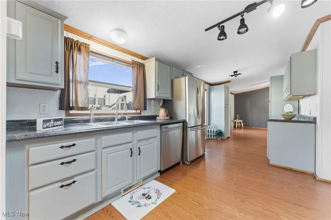 Kitchen featuring dark countertops, light wood-type flooring, gray cabinets, stainless steel dishwasher, and track lighting