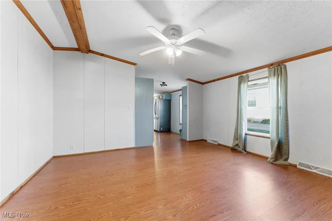 Unfurnished room featuring light wood-style flooring, ornamental molding, a ceiling fan, and a textured ceiling