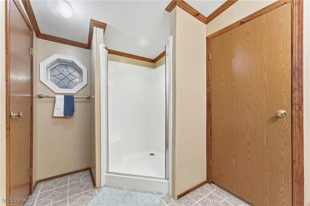 Bathroom with a shower stall, crown molding, and a textured ceiling