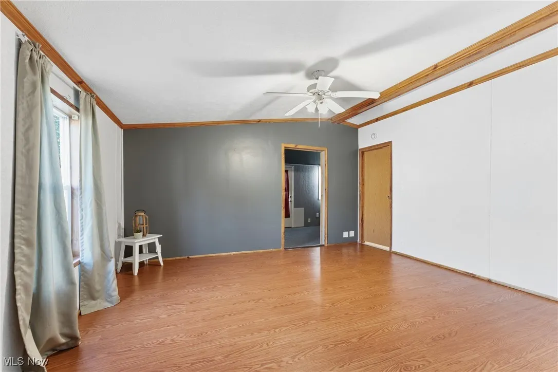 Empty room featuring crown molding, light wood-style flooring, a ceiling fan, and vaulted ceiling