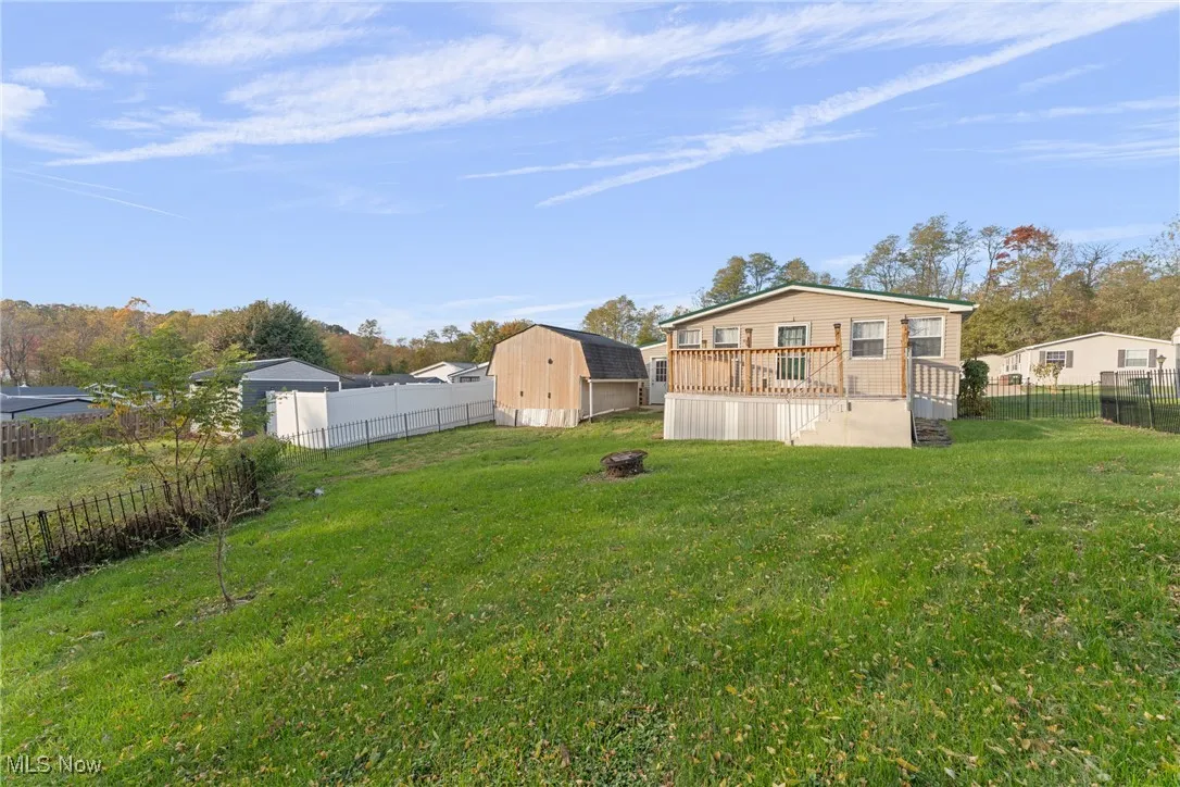 Fenced backyard featuring a wooden deck, a storage shed, and an outdoor fire pit