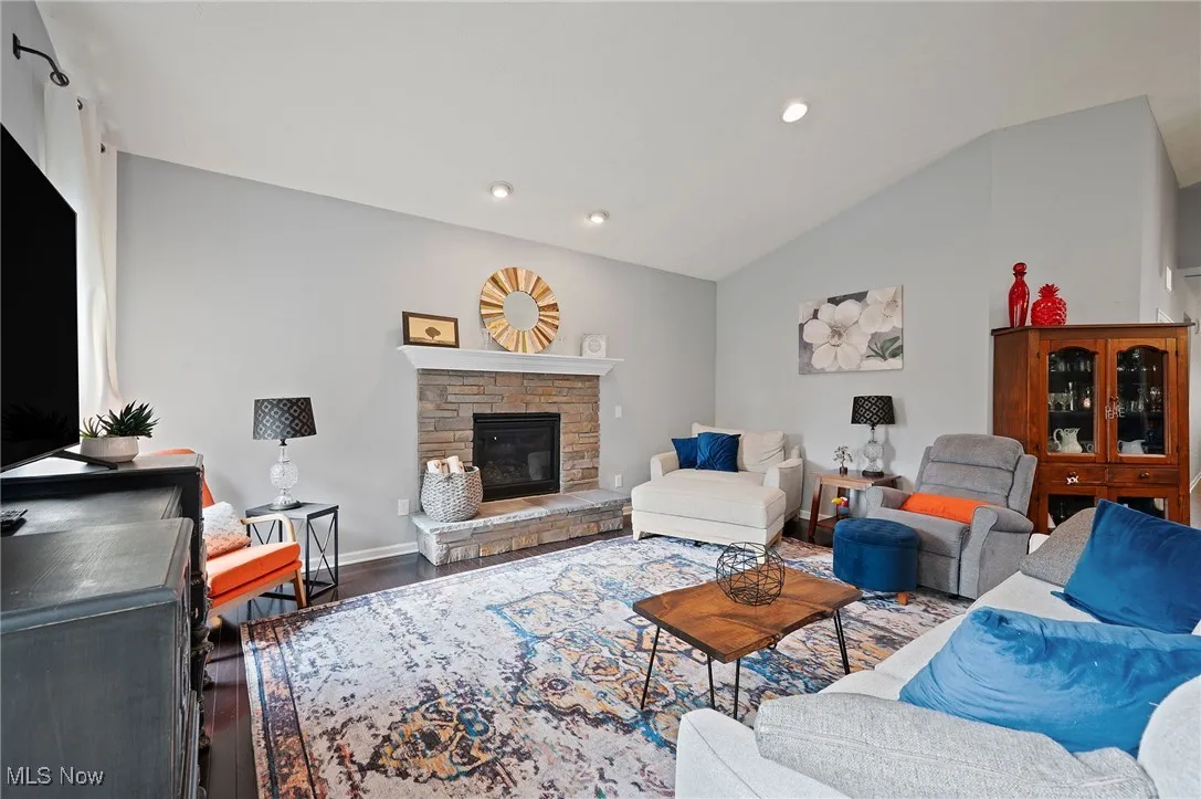 Living area with a stone fireplace, wood finished floors, vaulted ceiling, and recessed lighting