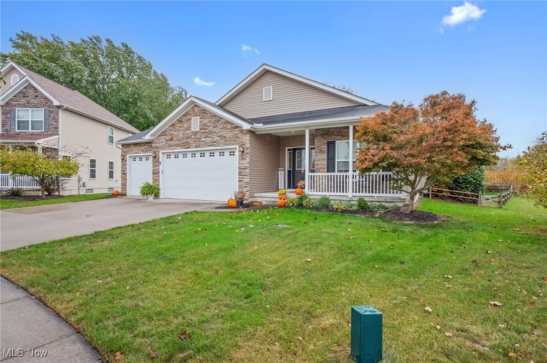 View of front of house featuring a porch, stone siding, driveway, a front lawn, and a garage
