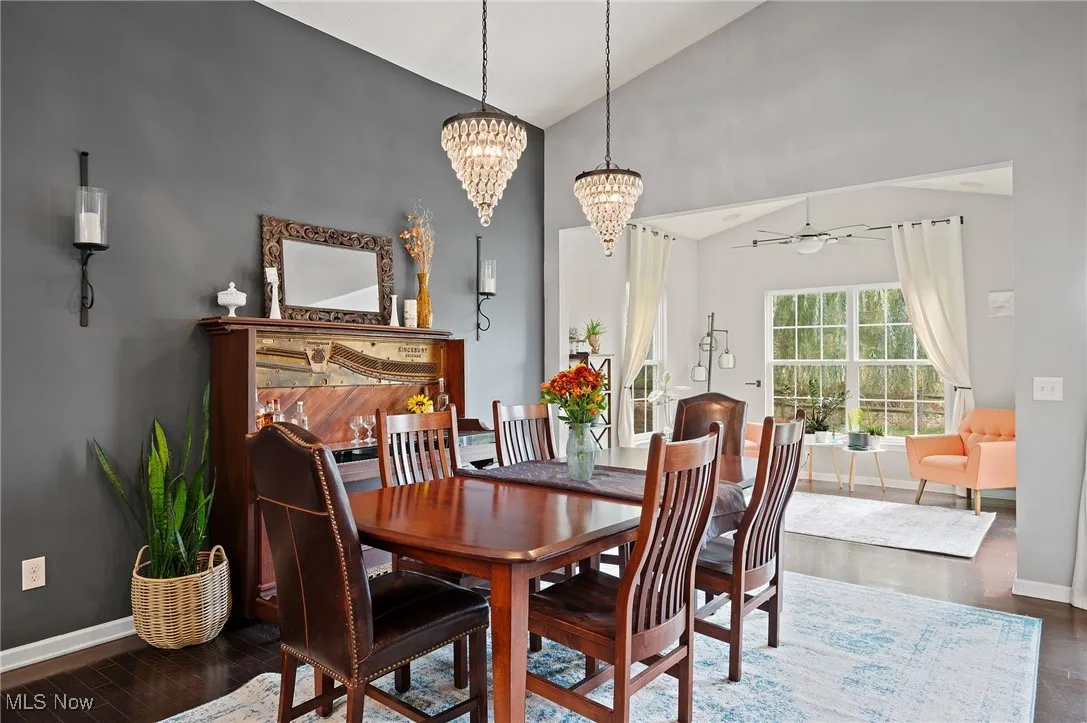 Dining area featuring dark wood-style flooring, ceiling fan, a chandelier, and high vaulted ceiling