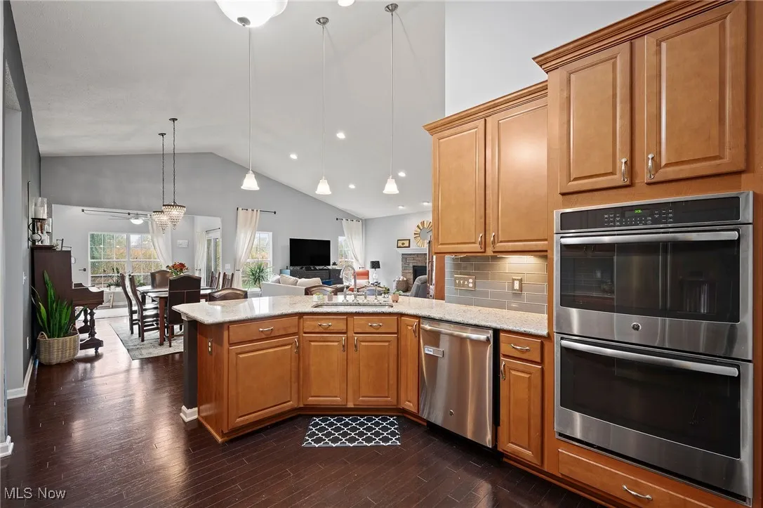 Kitchen with appliances with stainless steel finishes, a peninsula, open floor plan, tasteful backsplash, and decorative light fixtures