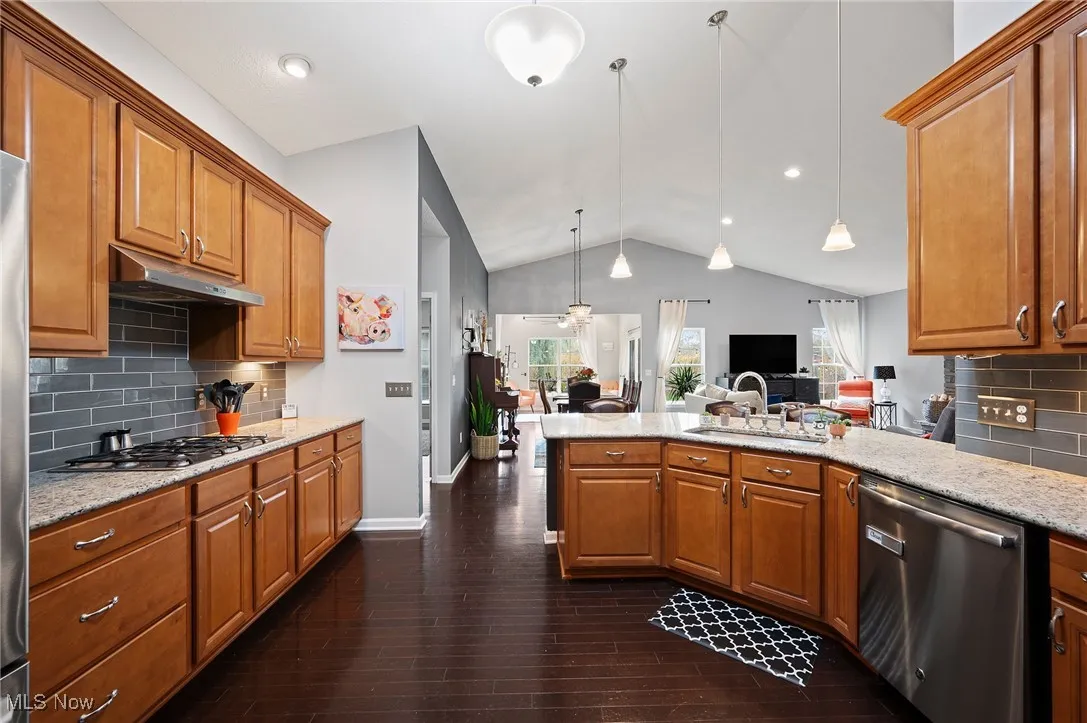 Kitchen featuring backsplash, brown cabinets, stainless steel appliances, hanging light fixtures, and light stone countertops